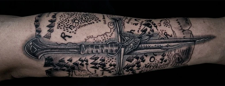 Detalhe de tatuagem em preto e cinza no braço com tema de senhor dos anéis